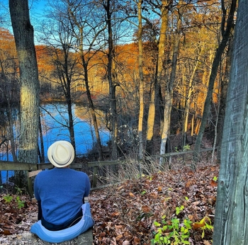 A man sits in an autumn forest in front of a body of water.