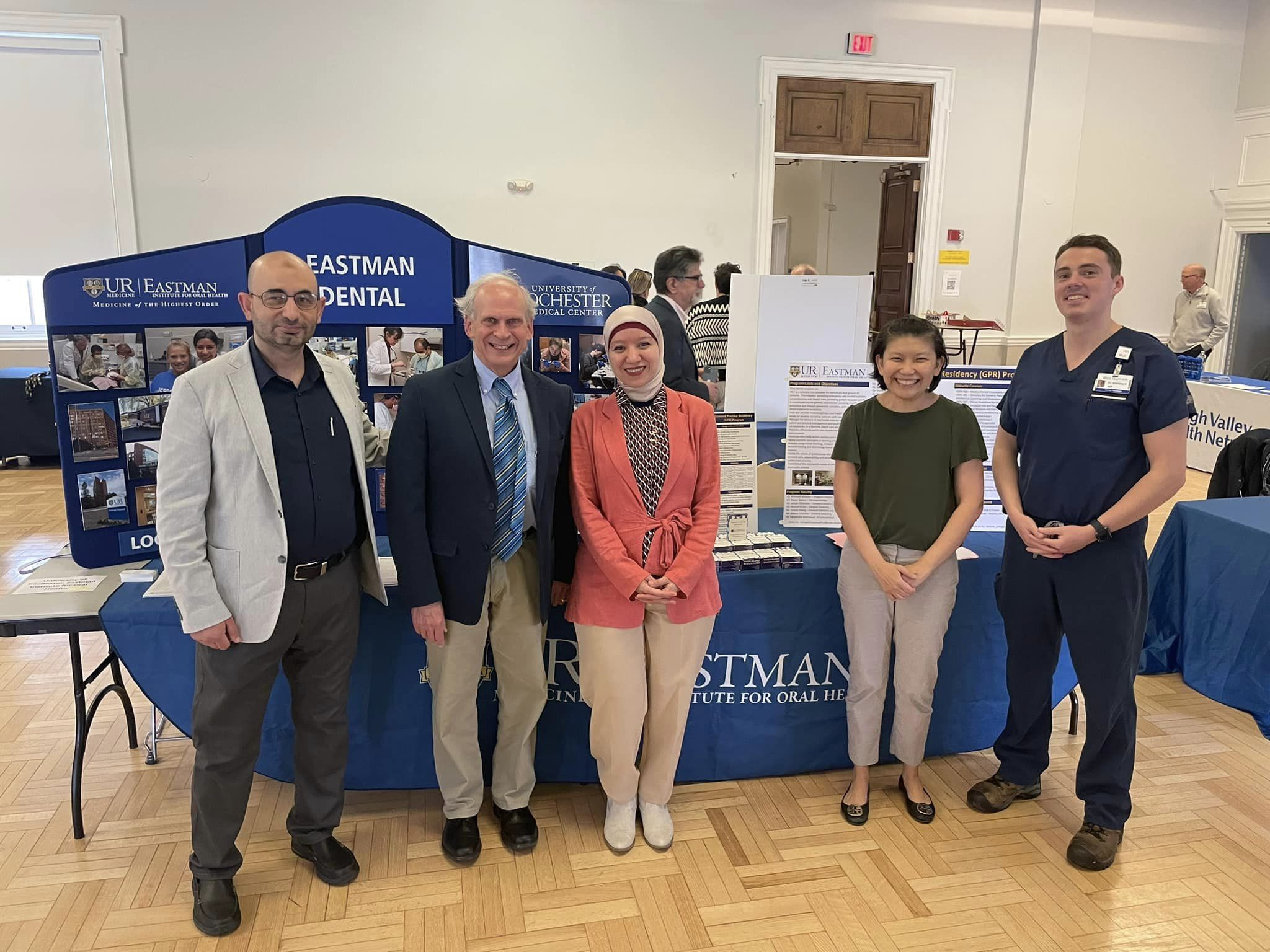 Five people stand in front of a table with multiple posters about Eastman Dental standing on it