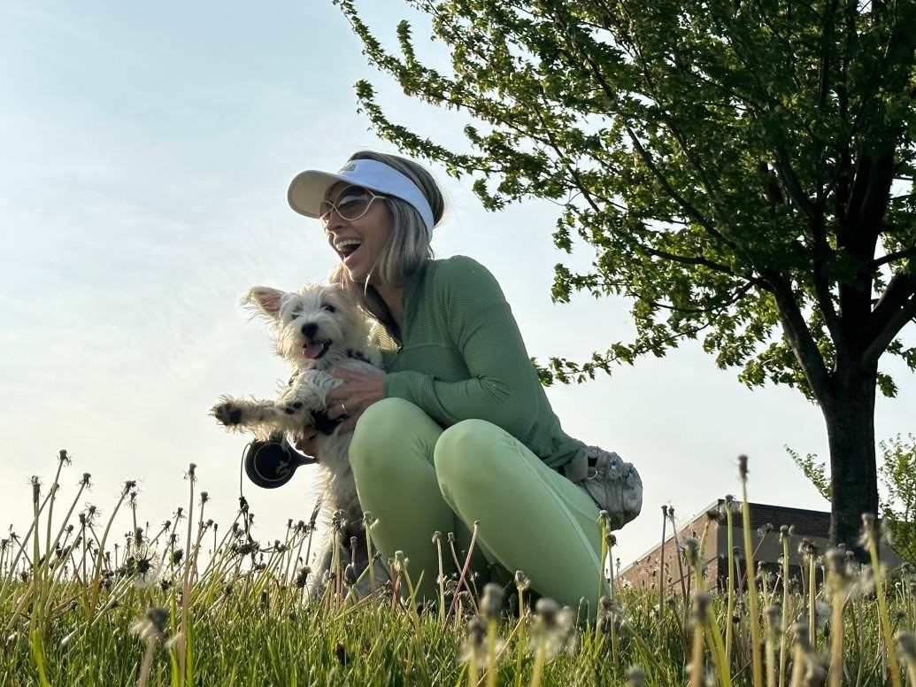 A woman plays in the grass with a happy, fluffy white dog.