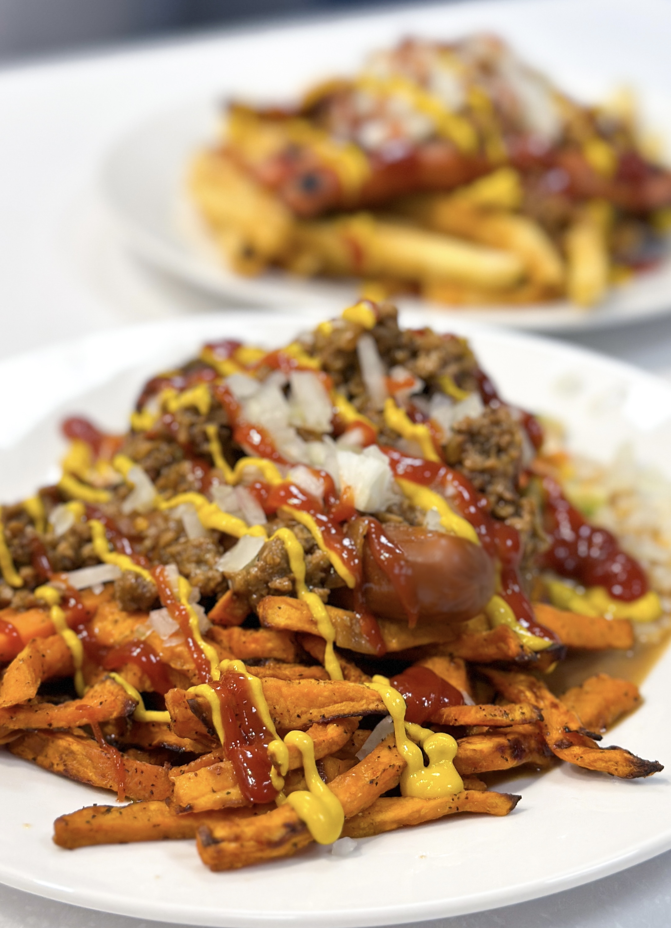 A plate with sweet potato fries, soy dogs, bean burger, vegetable salad, tofu hot sauce, mustard, ketchup and onions.