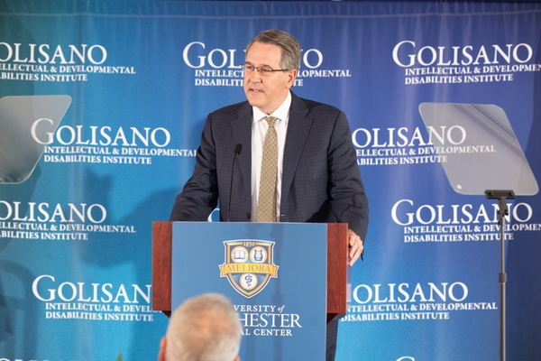 Dr. David Linehan stands at a podium in front of a banner that reads Golisano Intellectual and Developmental Disabilities Institute 