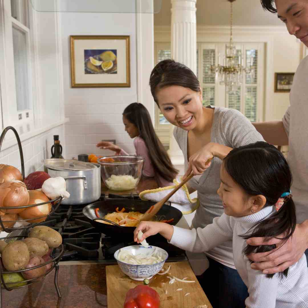 A mom smiles at her daughter who is helping her cook a meal full of vegetables in their home kitchen.