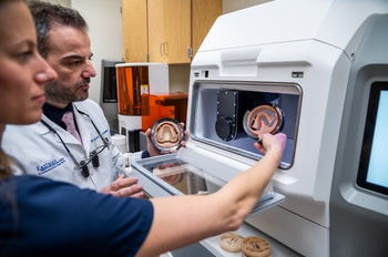 A person in scrubs and a person in a lab coat inspect jaw-shaped items that are being removed from a milling machine