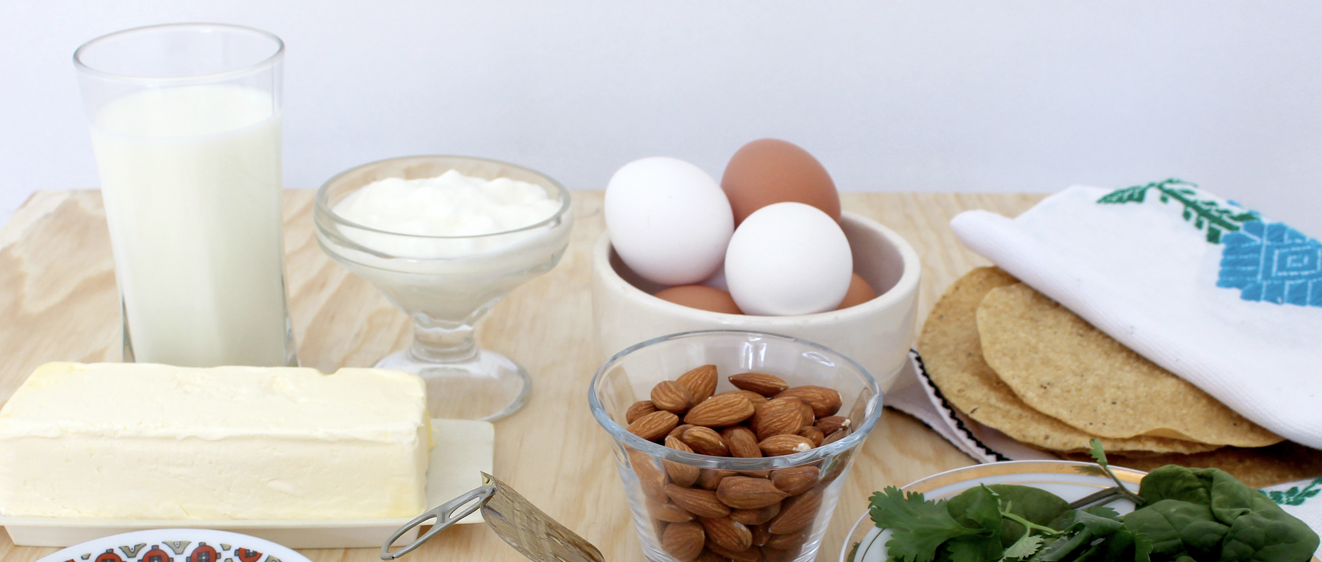 Foods full of calcium on a table, including eggs, milk, butter, almonds, and spinach.
