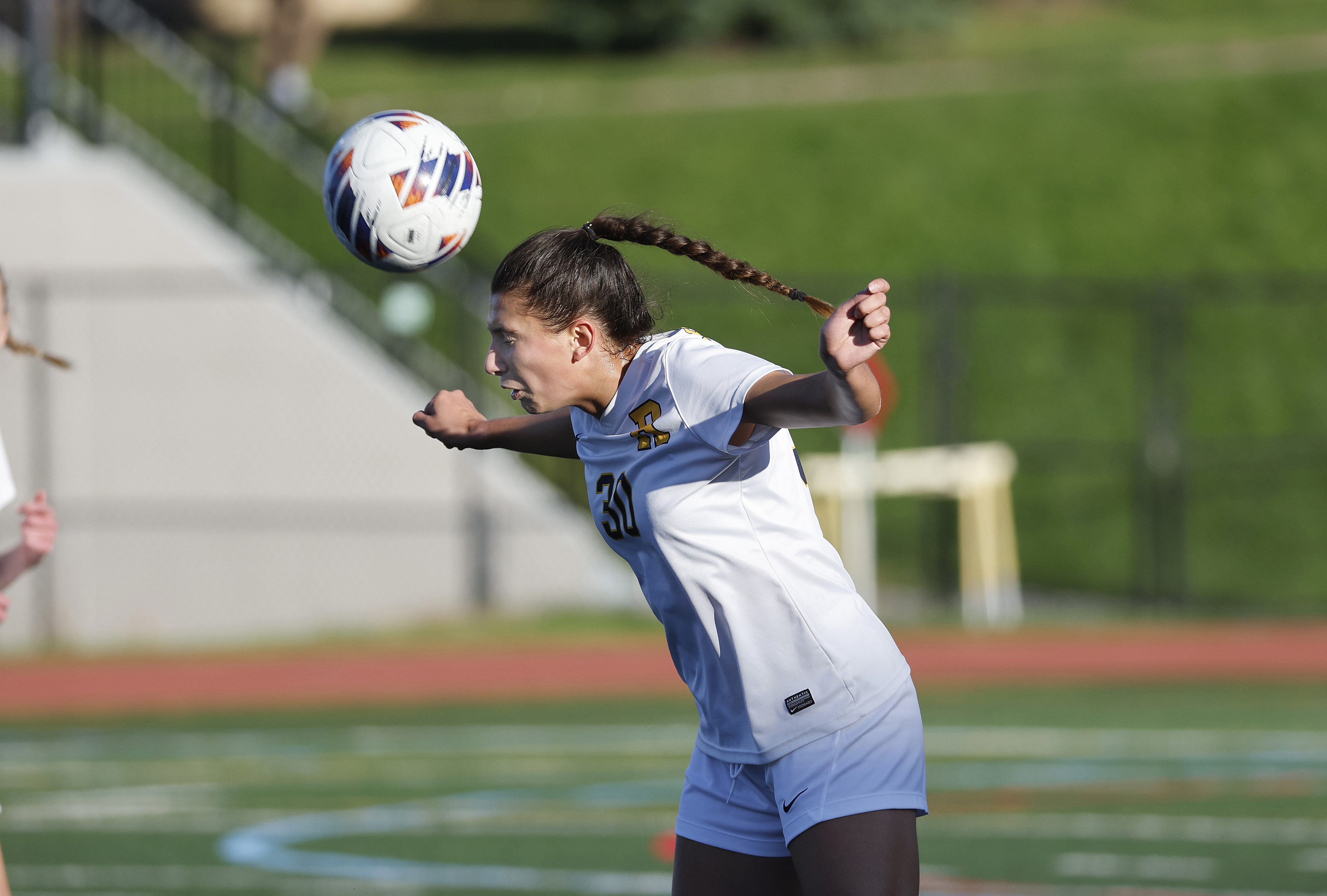 University of Rochester soccer player heads a ball during a game.