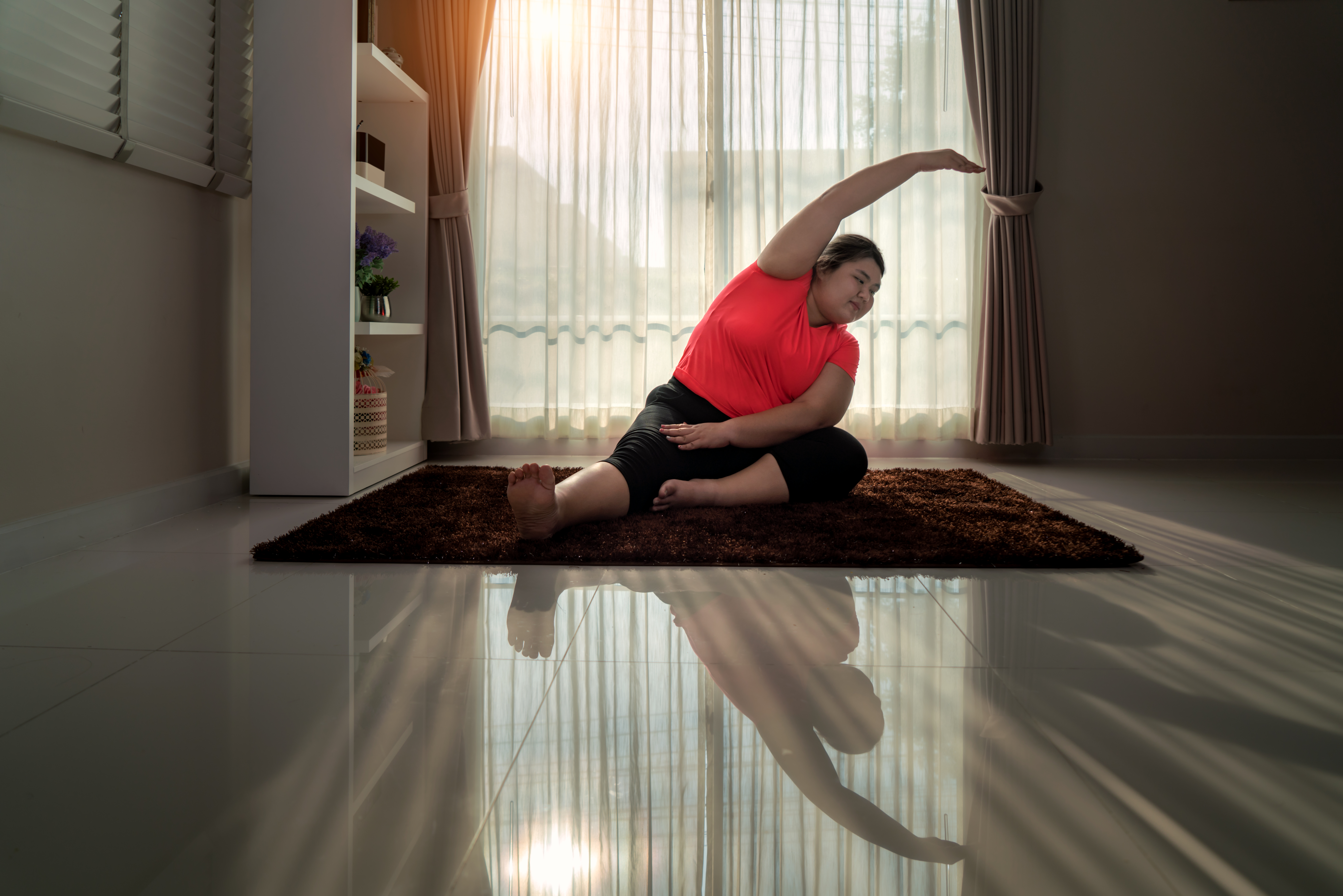A woman in a bright red top stretches on a yoga mat