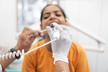 a patient opens their mouth as a dental professional uses a scanning device to check their teeth.