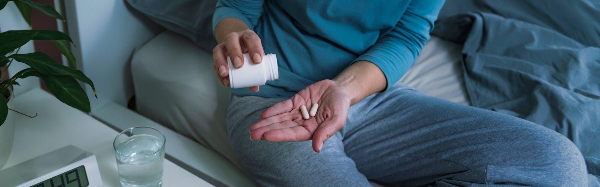 Close up of hands holding pill bottle of melatonin, shaking two supplements into their hand.