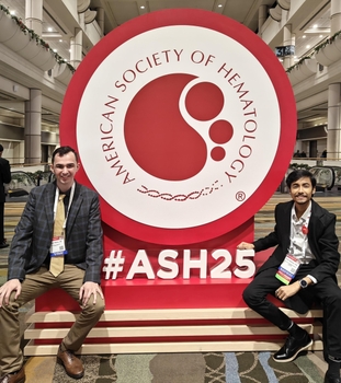 two male graduate students pose near a large sign at American Society of Hematology annual meeting