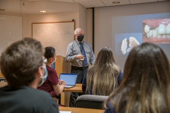 Dr. Saunders teaching a course, holds a powerpoint clicker as he explains a slide
