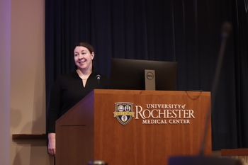 Dr. Sarah Crimmins stands behind a lectern with the University of Rochester Medical Center on its front