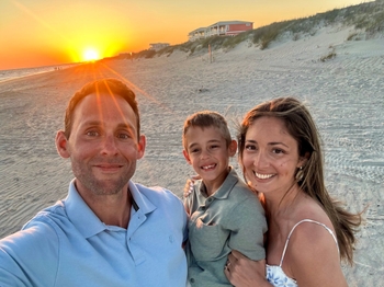 A young family poses along the beach at sunset.