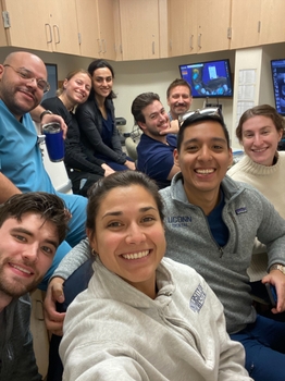 A group of people smile together. Desks and computers are visible in the background with dental images displayed.
