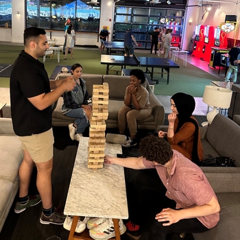 a group of people play jenga. Others play ping pong in the background