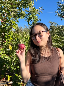 A woman smiles and holds an apple in an orchard.