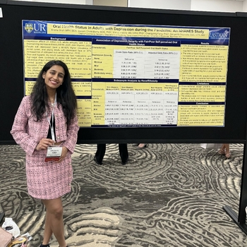 a woman in a pink skirt suit poses in front of a scientific paper.