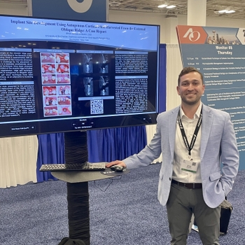 a man in a light blue suit poses next to a scientific poster displayed on a digital screen