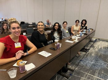 A group of people sit at a long desk in a lecture hall for a conference.