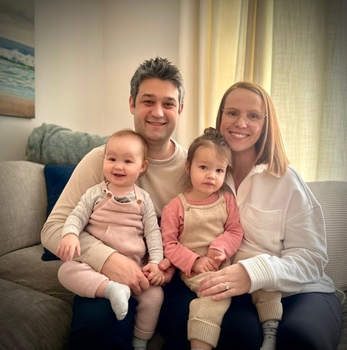 a man and a woman sit on a couch holding two young children on their laps.
