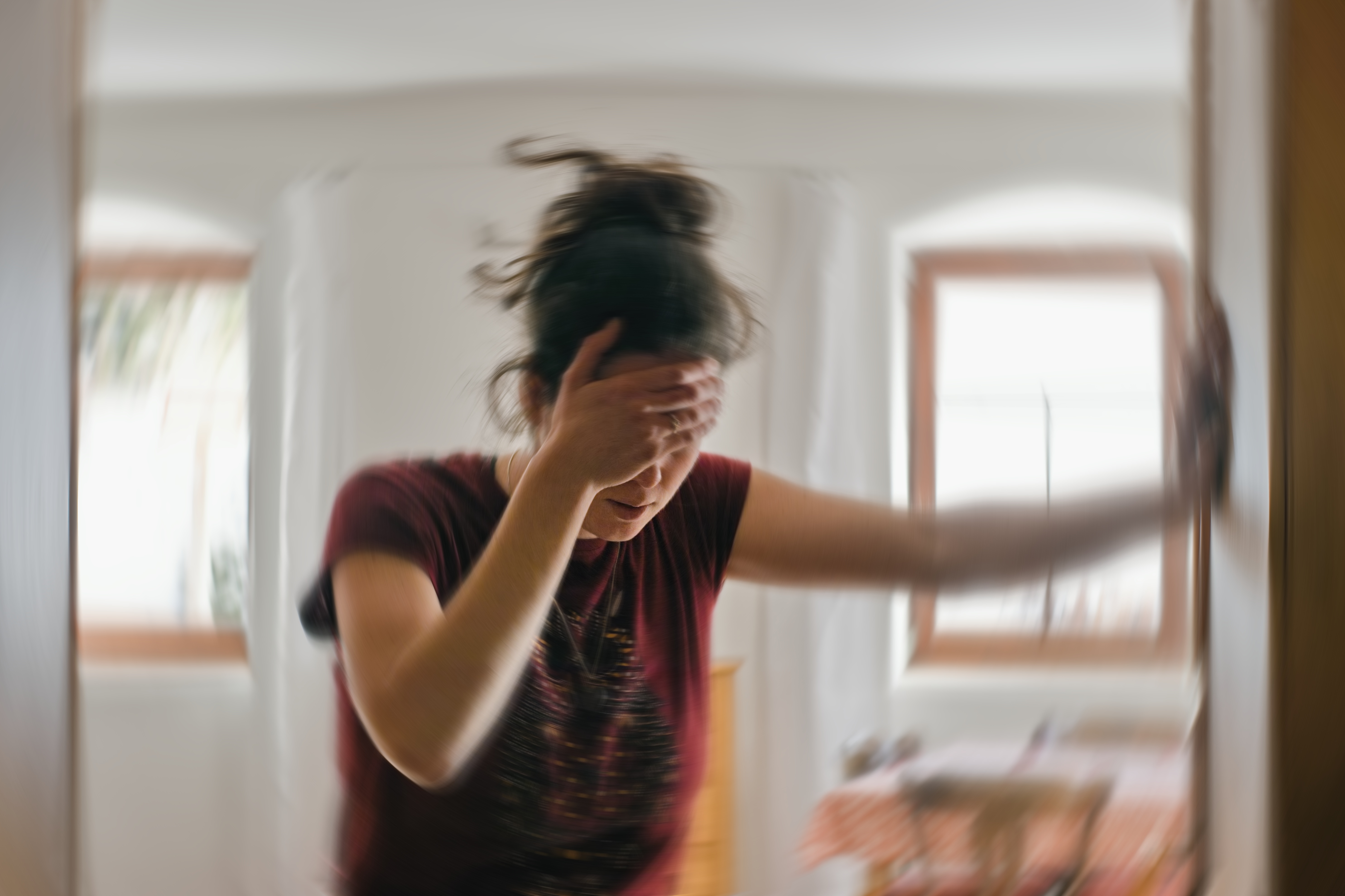 Woman with hand on head, leaning against wall while background appears blurred and swirling — illustration of feeling overwhelmed during an anxiety episode.