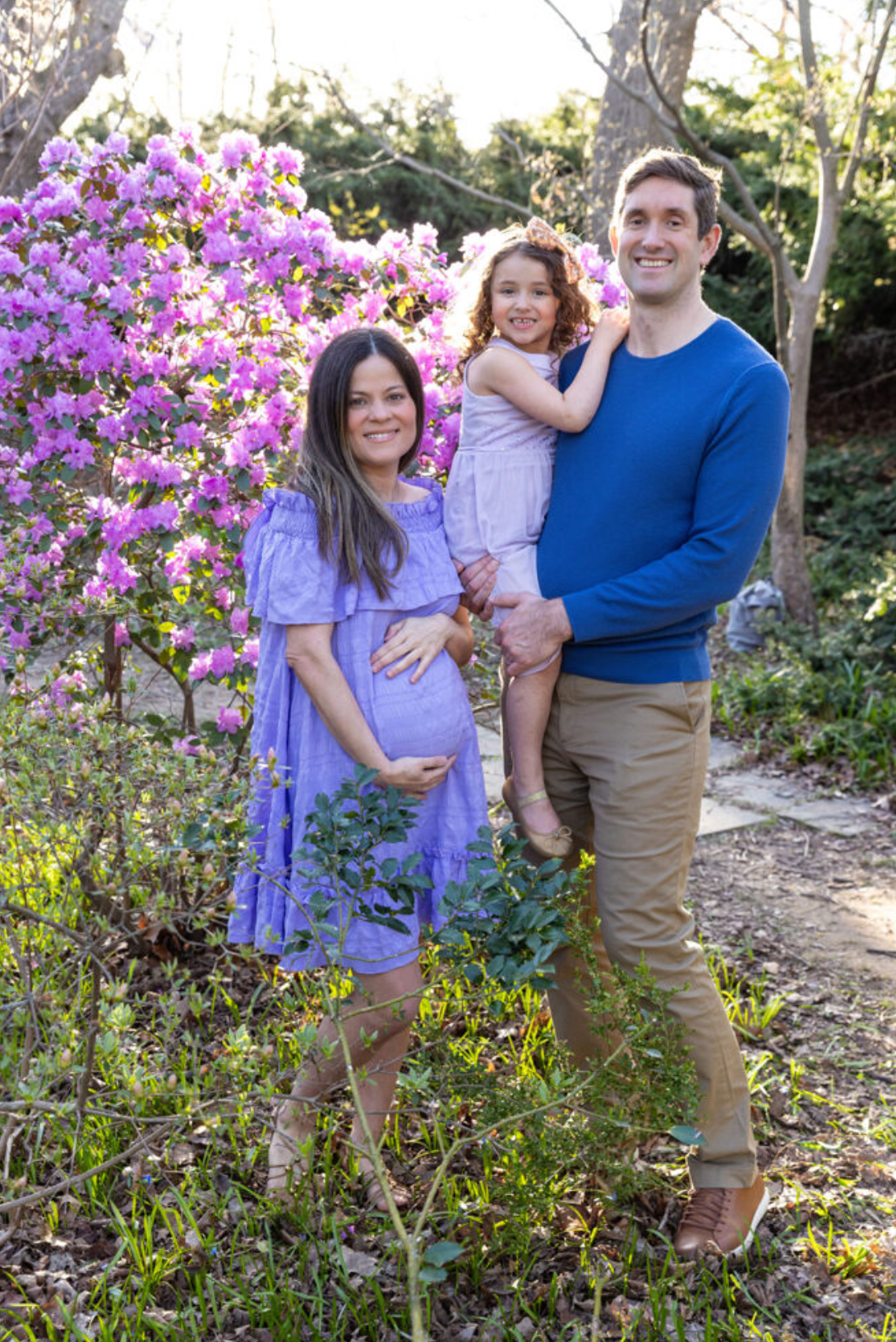 A pregnant woman smiles next to a man holding a young girl.