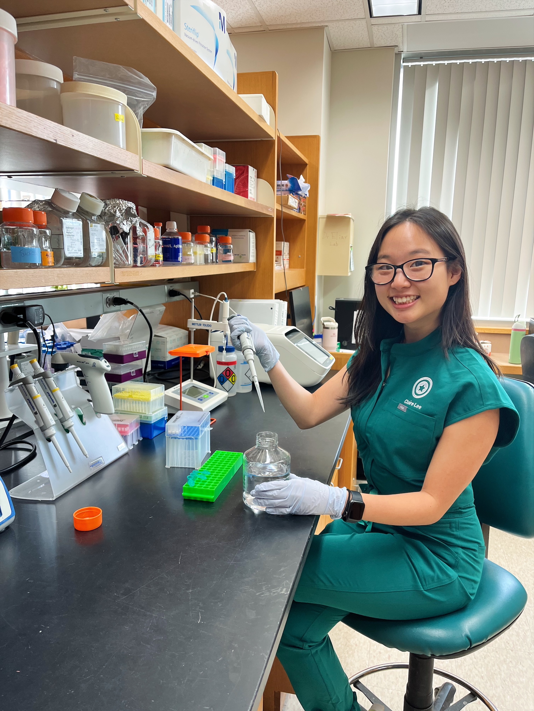 Claire Lee sits at a laboratory bench holding a pipette.