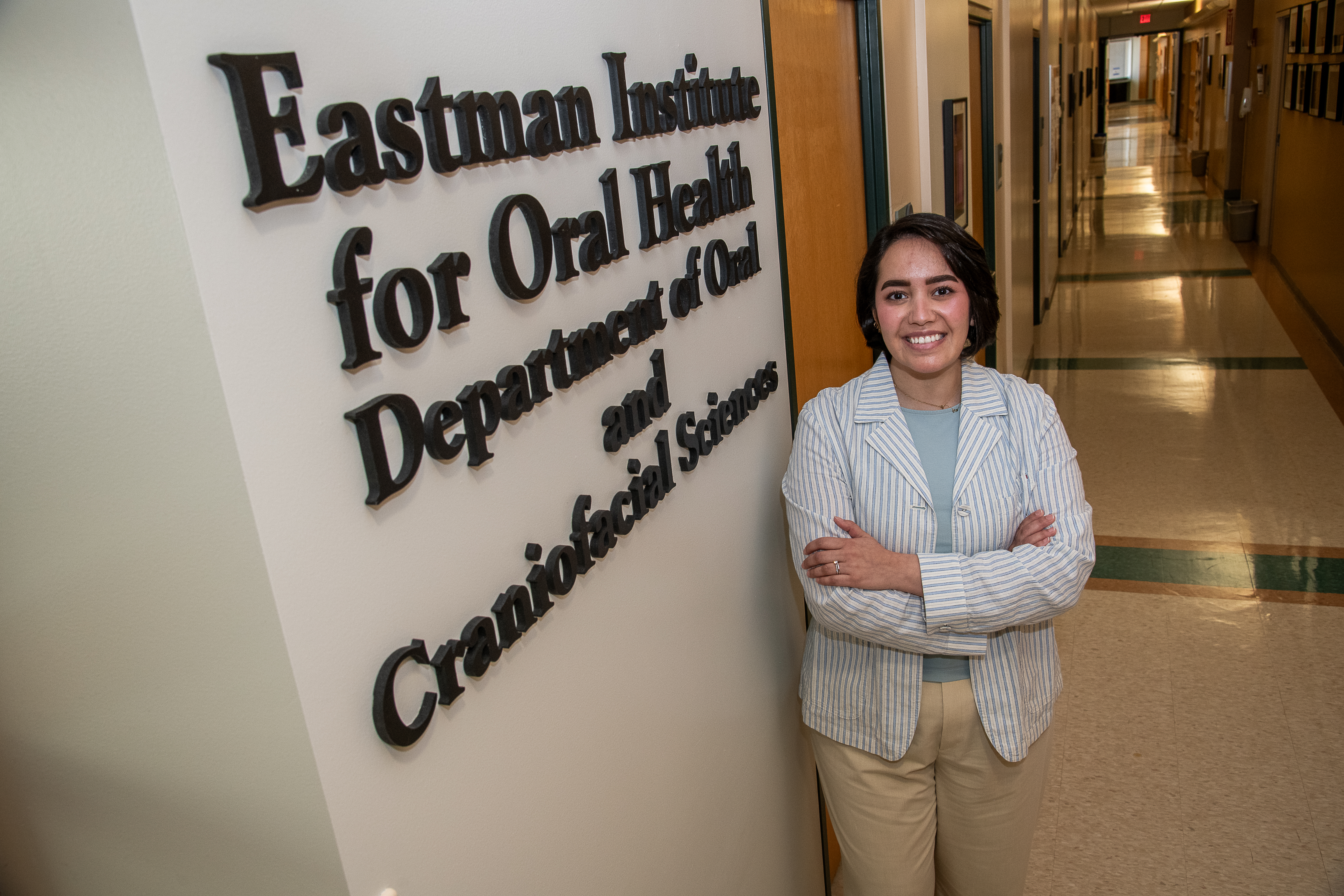 a woman in a white lab coat stands next to a wall that reads "Eastman Institute for Oral Health Department of Craniofacial Sciences