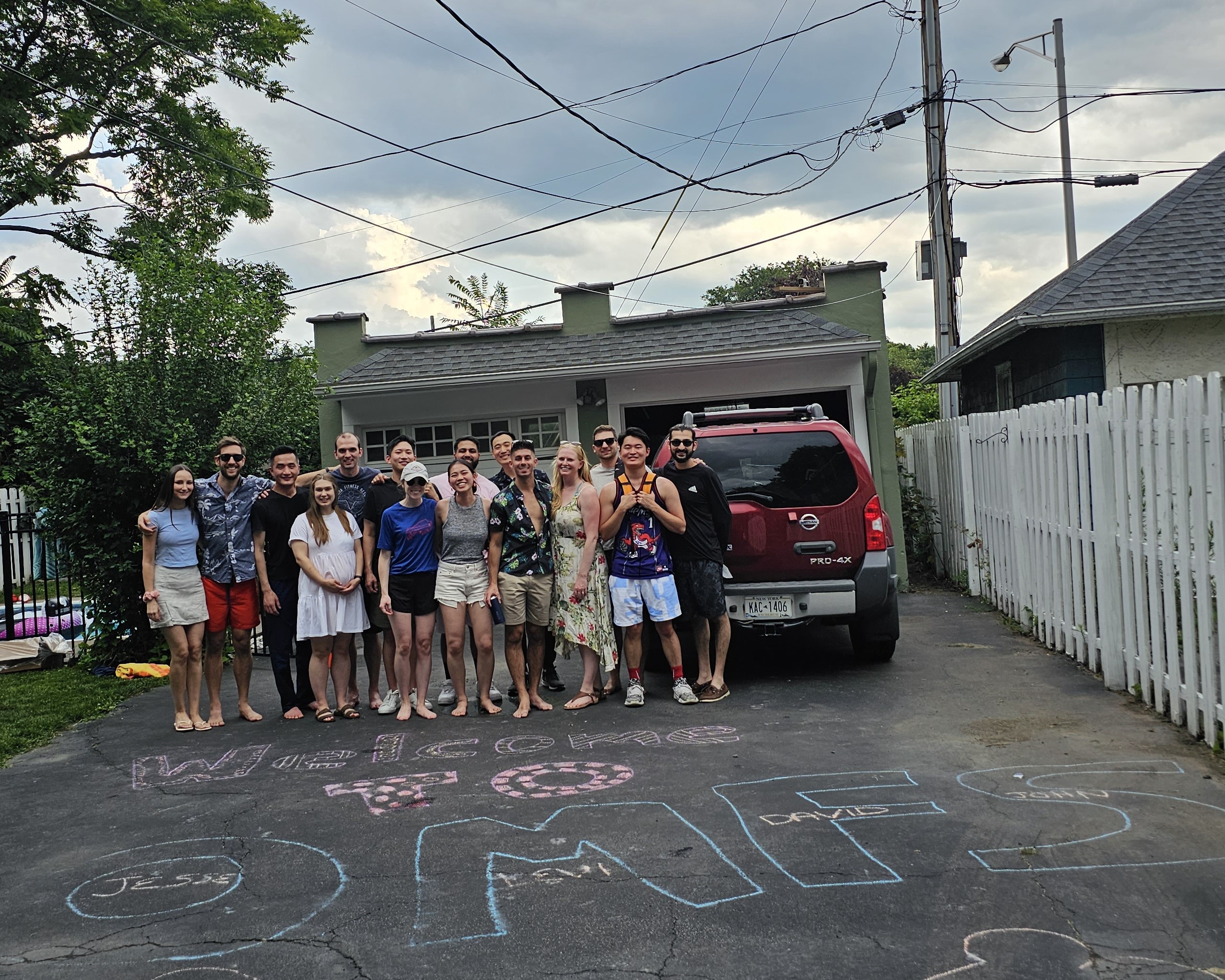 a group of people stand smiling in a driveway behind chalk art reading "Welcome to OMFS".