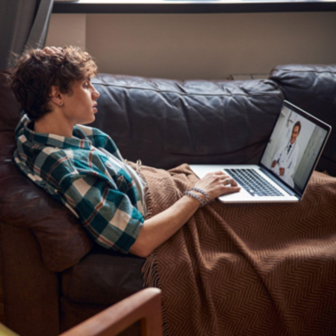 Man on couch in a virtual urgent care visit on his laptop
