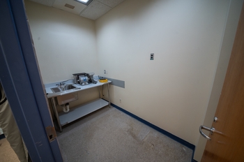 a small room that contains only a small metal bench with a sink. The counter is partly covered in peeling laminate, and holds a few small machines.