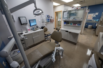 two light tan chairs are on either side of a brand-new light tan dental chair. The dental tray and lamp are white and shiny.