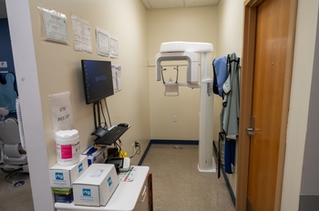 a new x-ray machine is in a small enclosed space, facing a back wall. A cabinet stands to the left. A door on the right has trim painted yellow. The surrounding walls are painted cream.