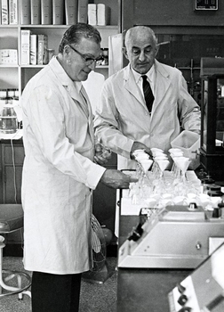 Two men in lab coats set up glass flasks on a laboratory bench.