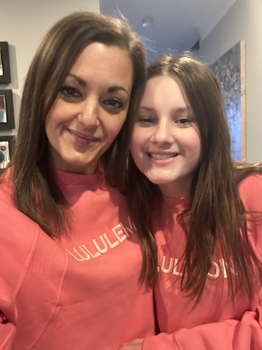 A woman and her daughter smile together wearing matching pink sweatshirts.