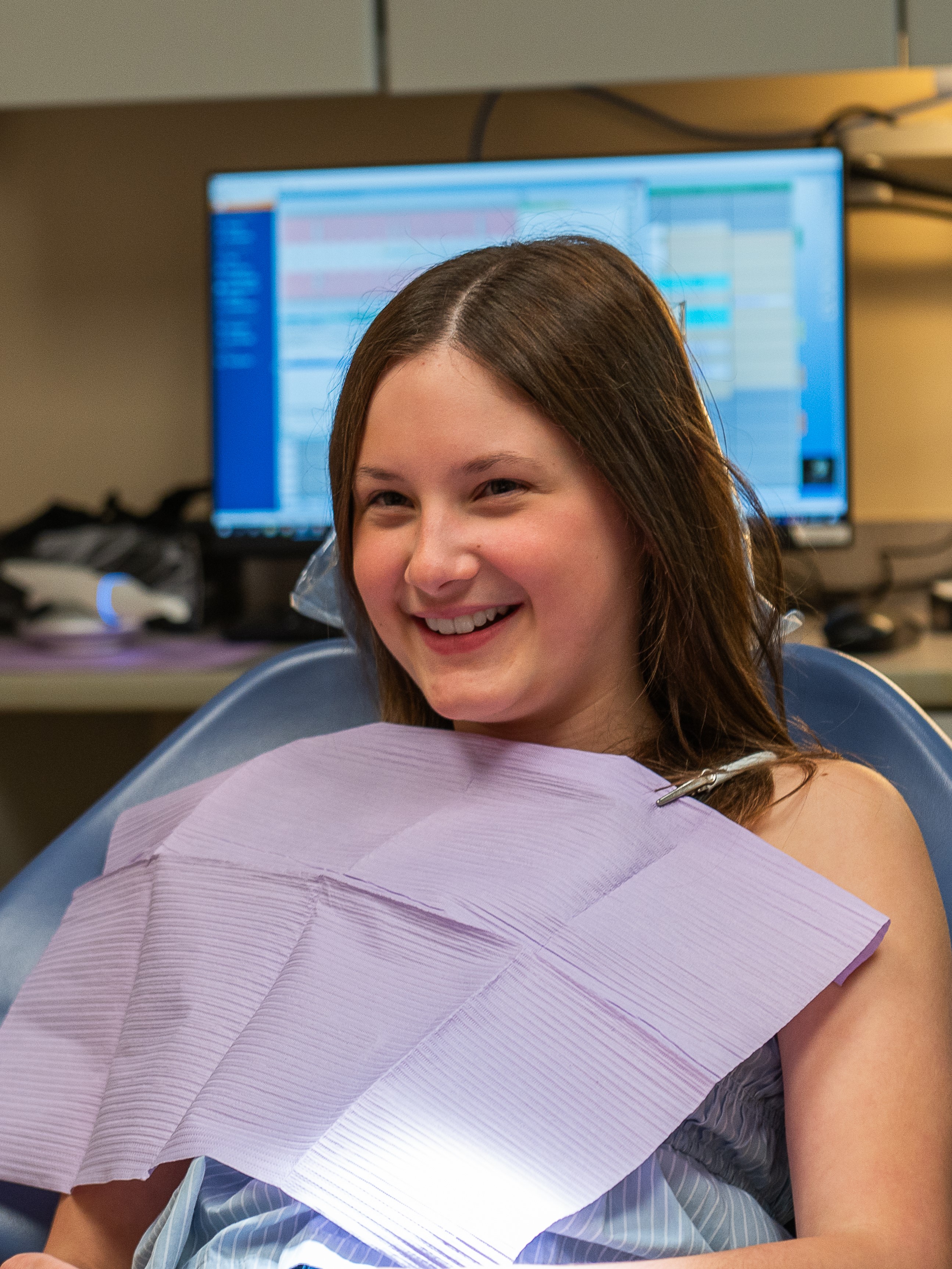 a girl sits in a dental chair, smiling.