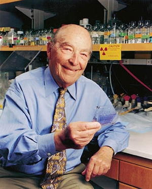 Dr. Arthur Kornberg smiles in a lab wearing a blue shirt and a yellow tie