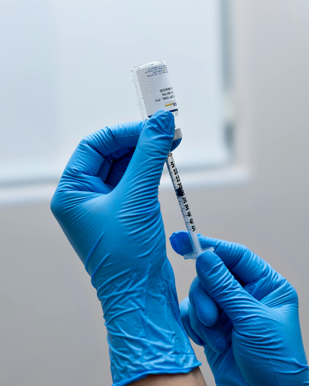 Hands wearing gloves prepare vaccine from vial