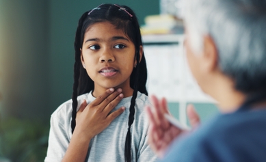 young girl holding her throat, talking to doctor