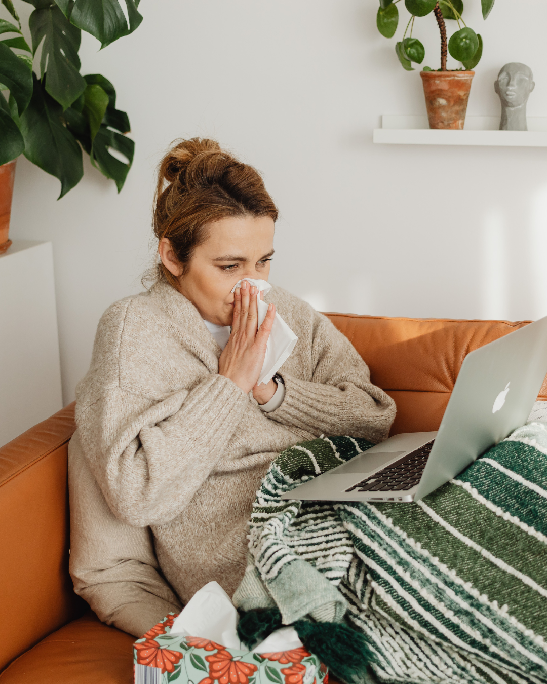 Woman holds tissue while looking at computer for Virtual Urgent Care with UR Medicine for flu symptoms