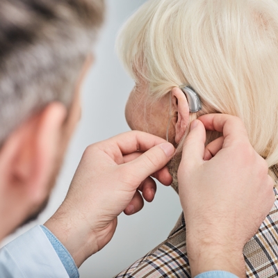 older woman having a hearing aid put on or adjusted by a doctor