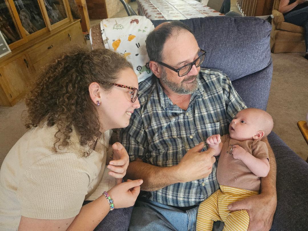 Robert Oman holding his new grandson while his grown granddaughter looks on. 