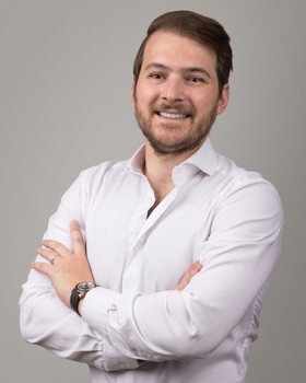 A portrait of Dr. Tavelli, smiling with his arms folded.