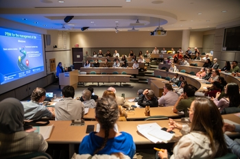 A view of a past Oral Medicine Conference. A large lecture hall filled with people listening to a talk.