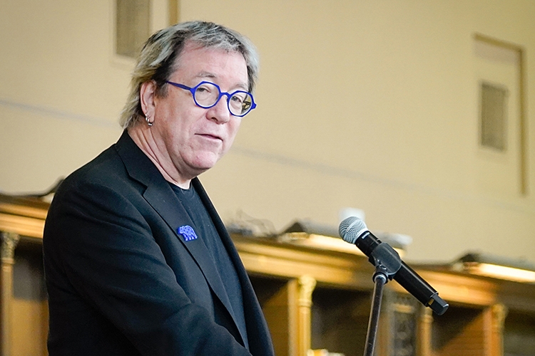 Jeffrey MacKie-Mason, the University Librarian, looks toward the camera while standing at a podium giving a presentation. He is wearing eyeglasses with blue frames and a Cal bear pin.