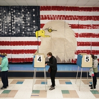 three people voting in a gymnasium with a giant painting of an American flag with an eagle head on the wall to their side