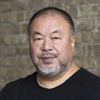 Portrait of a man with short hair and beard with a serious look on his face with a brick wall in the background