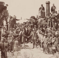 a black-and-white photo of about 100 white men in hats shaking hands and celebrating, some of  whom are on top of a train