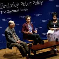 three people sit on a stage and speak to an audience