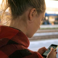 A stock photo of a person in a plaid hoodie looking at a cell phone