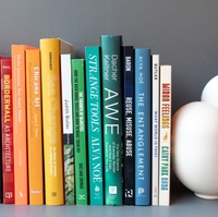 about a dozen book spines are lined up next to each other with a vase at one end